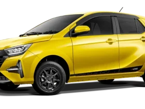 Mobil Daihatsu Ayla berwarna kuning cerah, diparkir di luar ruangan dengan latar belakang pepohonan hijau.
